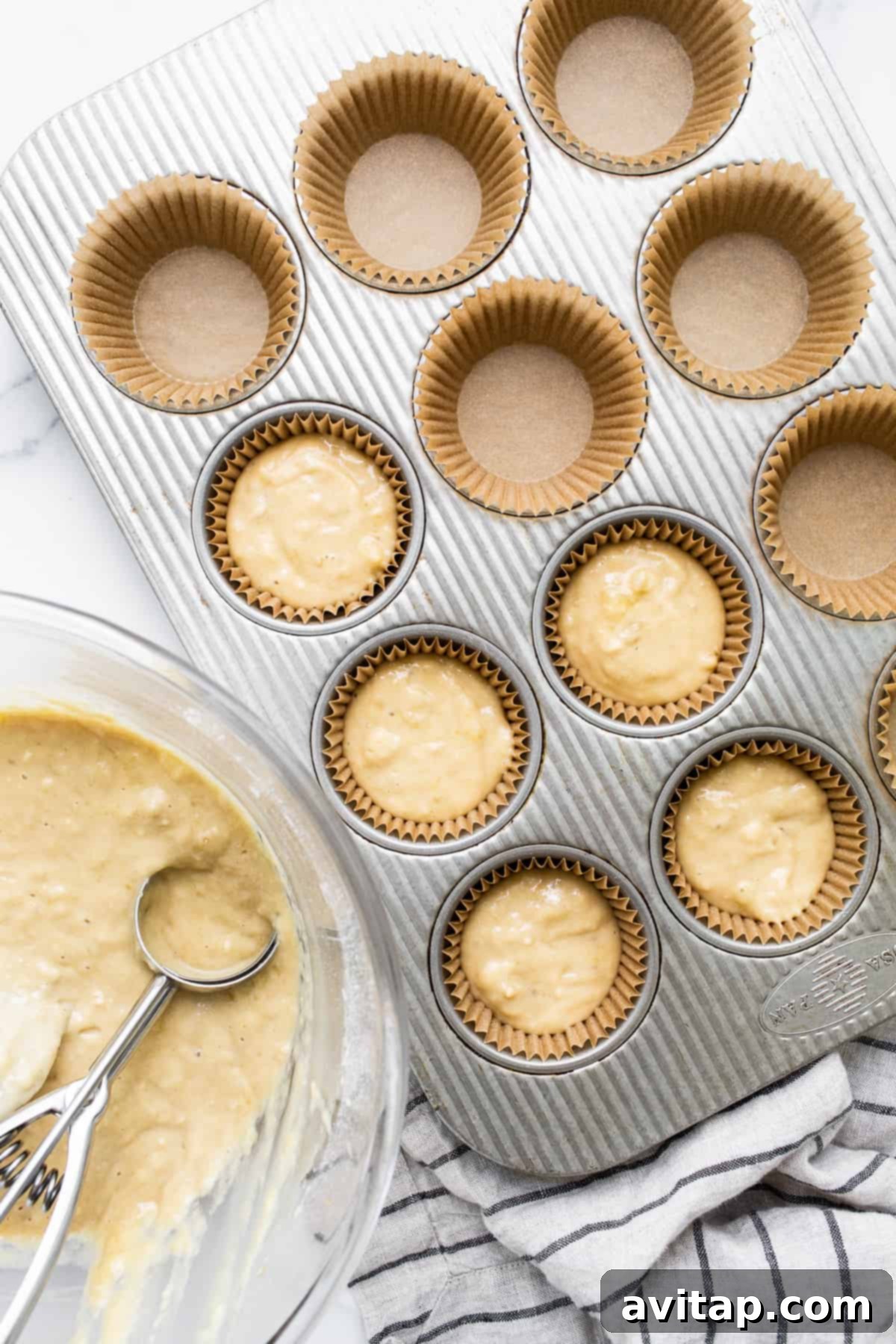 Muffin batter in liners, ready for baking. Muffin tin lined with paper liners and filled with smooth banana bread batter, ready for the oven.