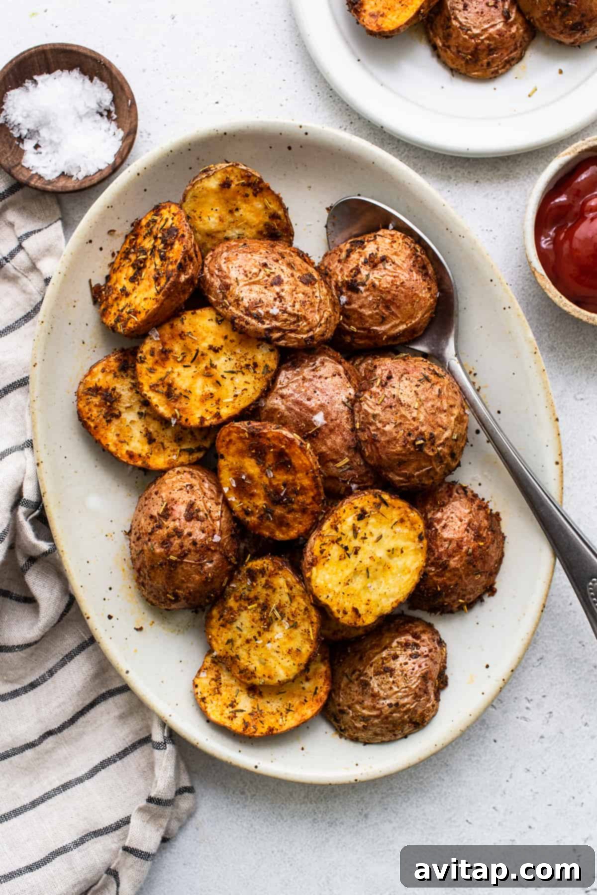 Serving Crispy Air Fryer Potatoes A bowl of crispy air fryer potatoes served on a plate with a spoon, showing their golden brown texture and fluffy interior.