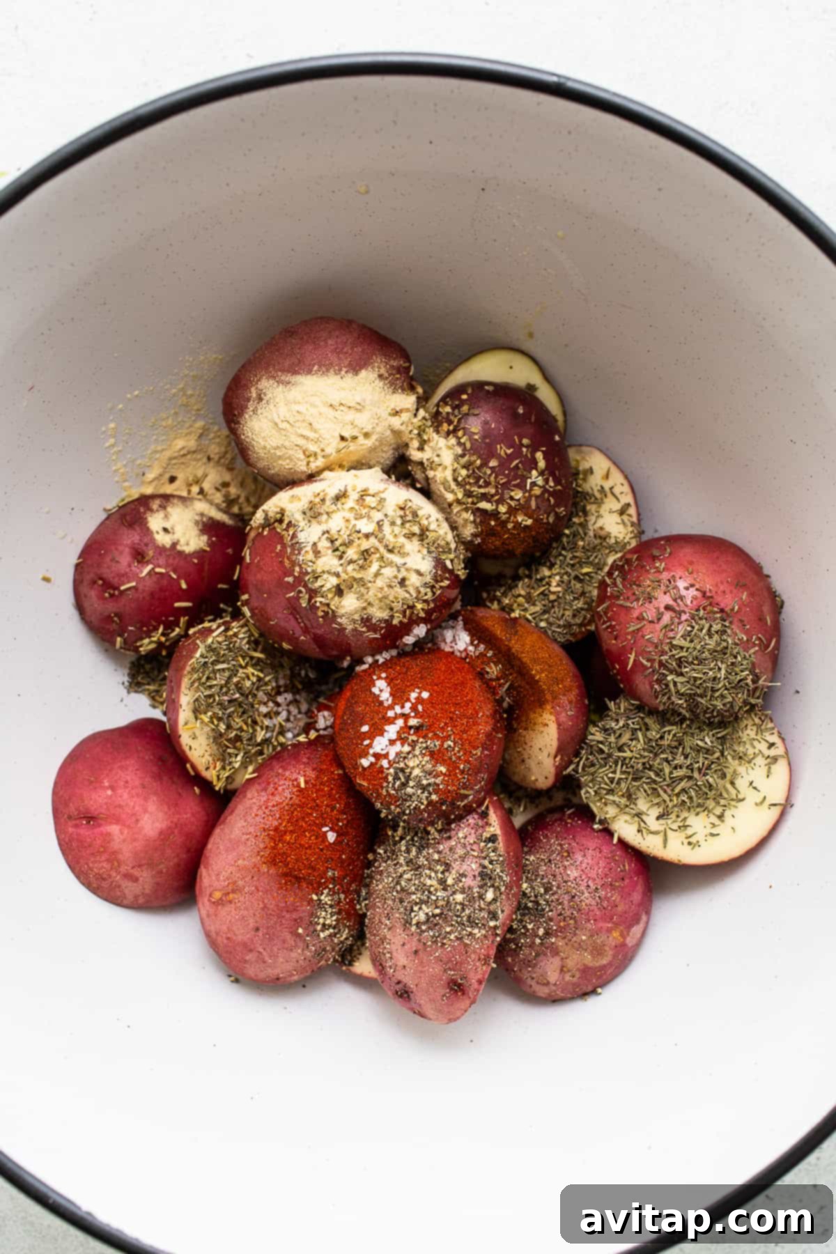 Seasoning Your Air Fryer Potatoes to Perfection Baby red potatoes in a bowl, tossed with olive oil and a vibrant blend of seasonings, ready for the air fryer.