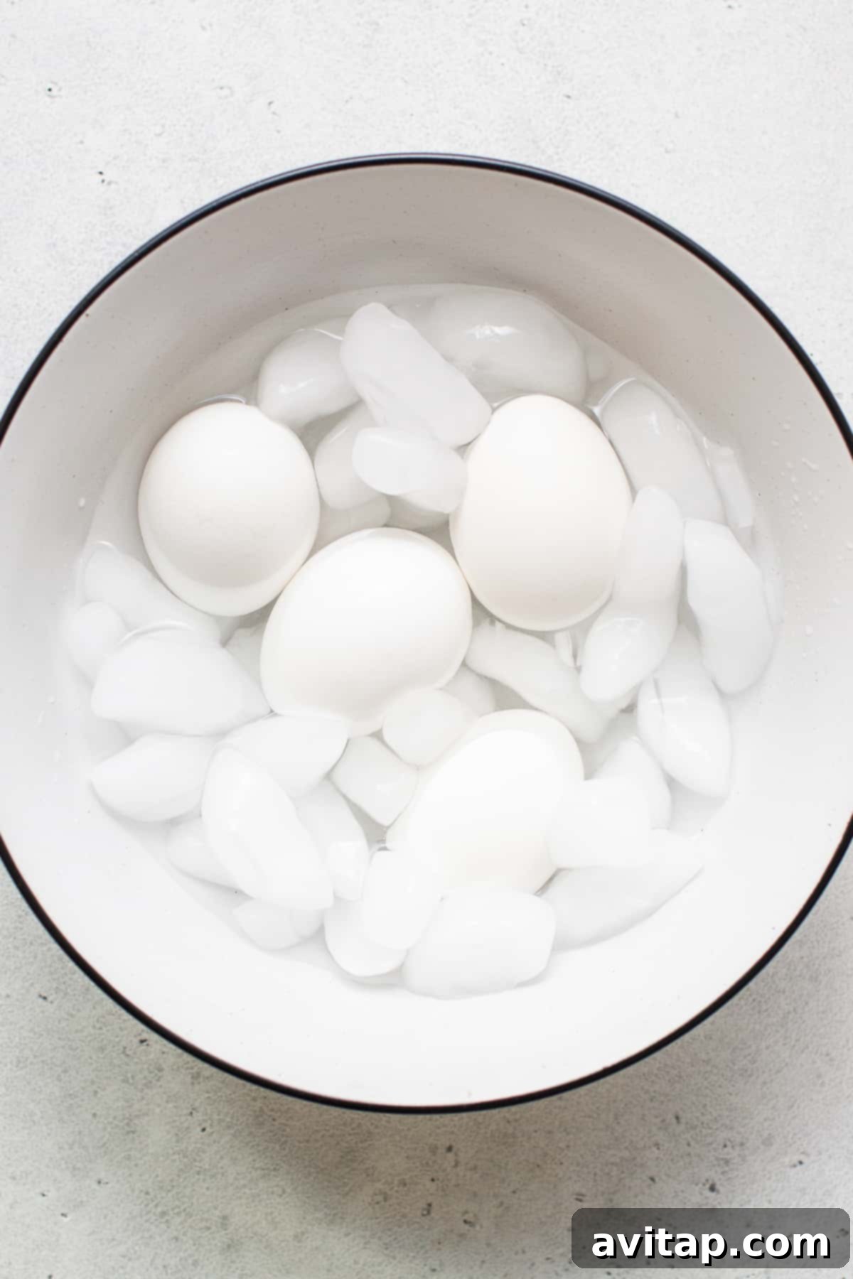 Soft boiled eggs chilling in a bowl with ice, prepared for the ice bath to stop the cooking process.