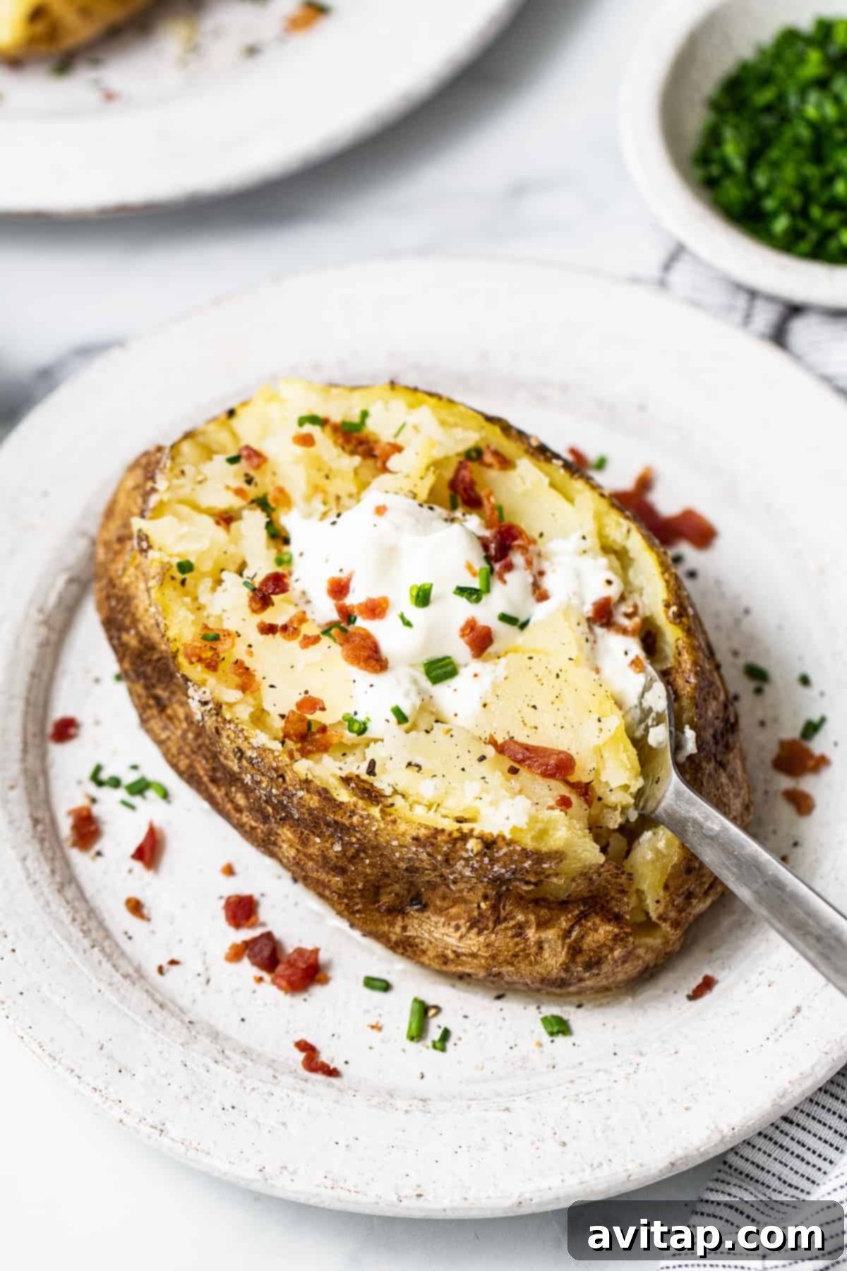 Perfect Microwave Baked Potato 4 A freshly microwaved potato topped generously with sour cream, fresh chives, and crispy bacon bits, ready to be enjoyed.