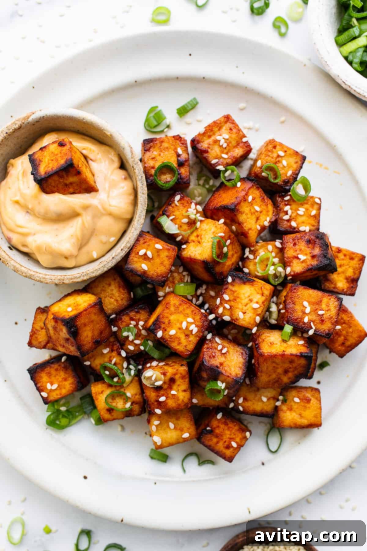 Crispy Air Fryer Tofu 2 Crispy air fryer tofu served on a plate, garnished with sesame seeds and green onions, accompanied by a creamy chili sauce dip.