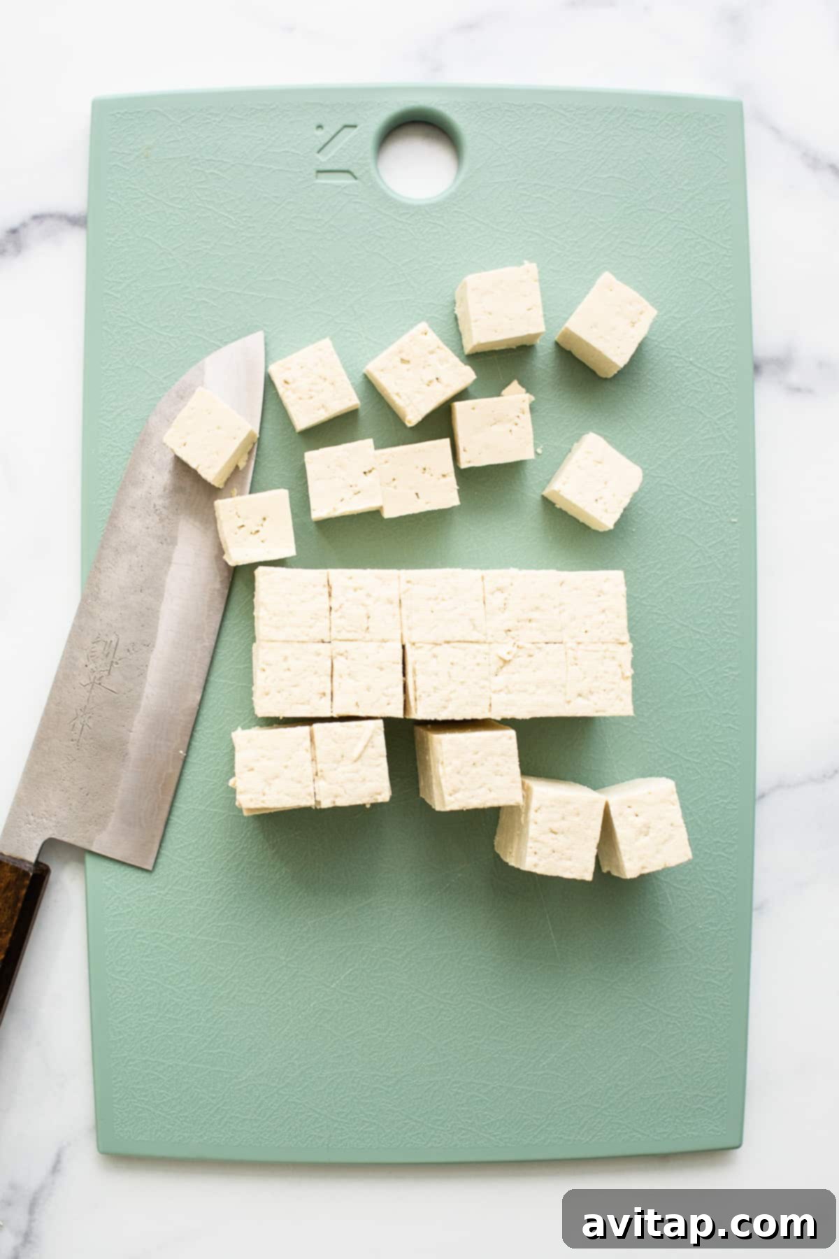 Crispy Air Fryer Tofu 3 Slicing a block of tofu into uniform cubes on a cutting board, preparing it for marination.