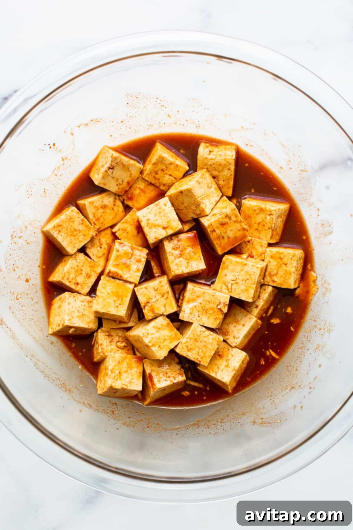 Crispy Air Fryer Tofu 4 Tofu cubes soaking in a vibrant red gochujang marinade in a bowl, absorbing flavors.