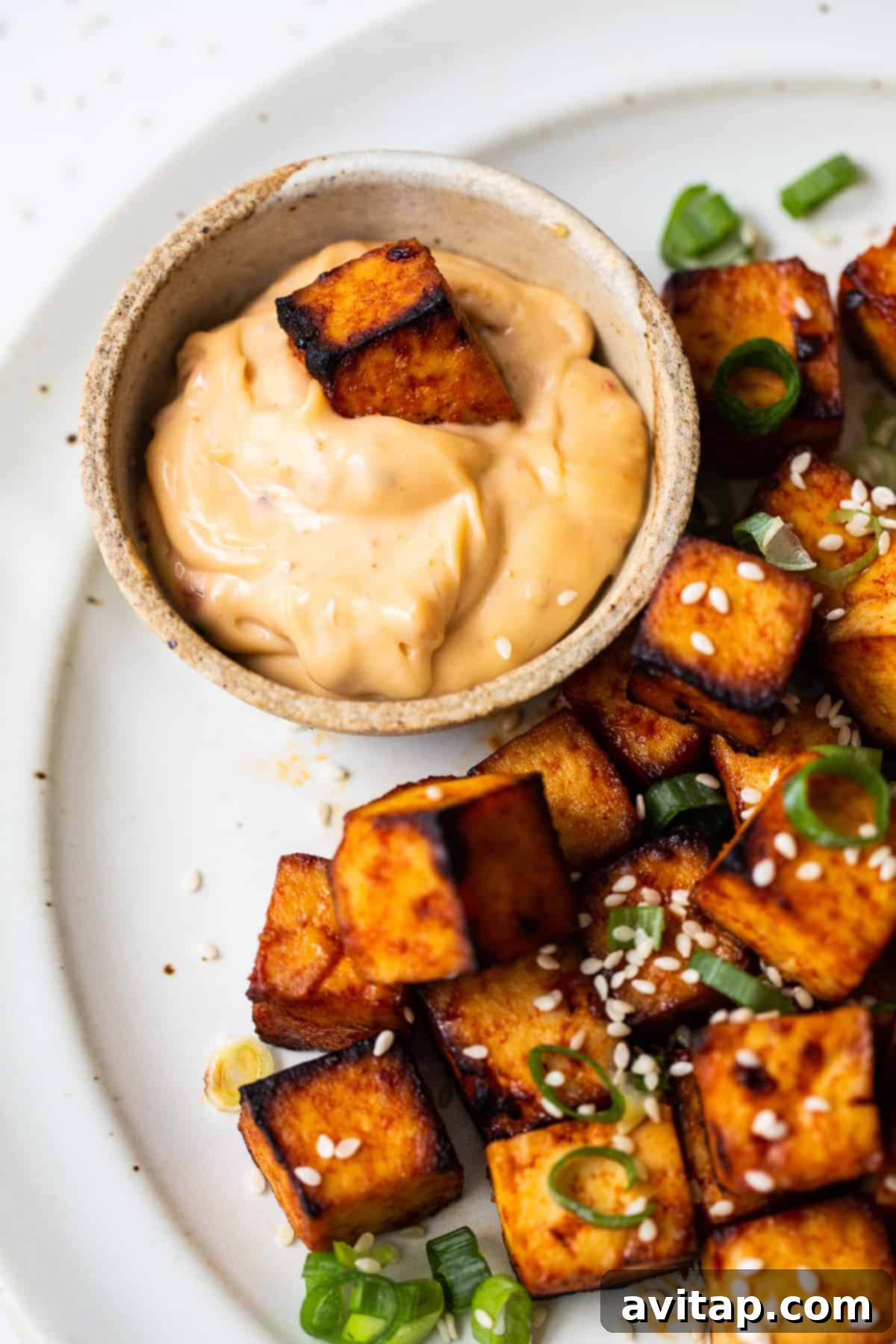 Crispy Air Fryer Tofu 7 A close-up of a perfectly crisped piece of air fryer tofu being dipped into a rich, creamy spicy sauce.