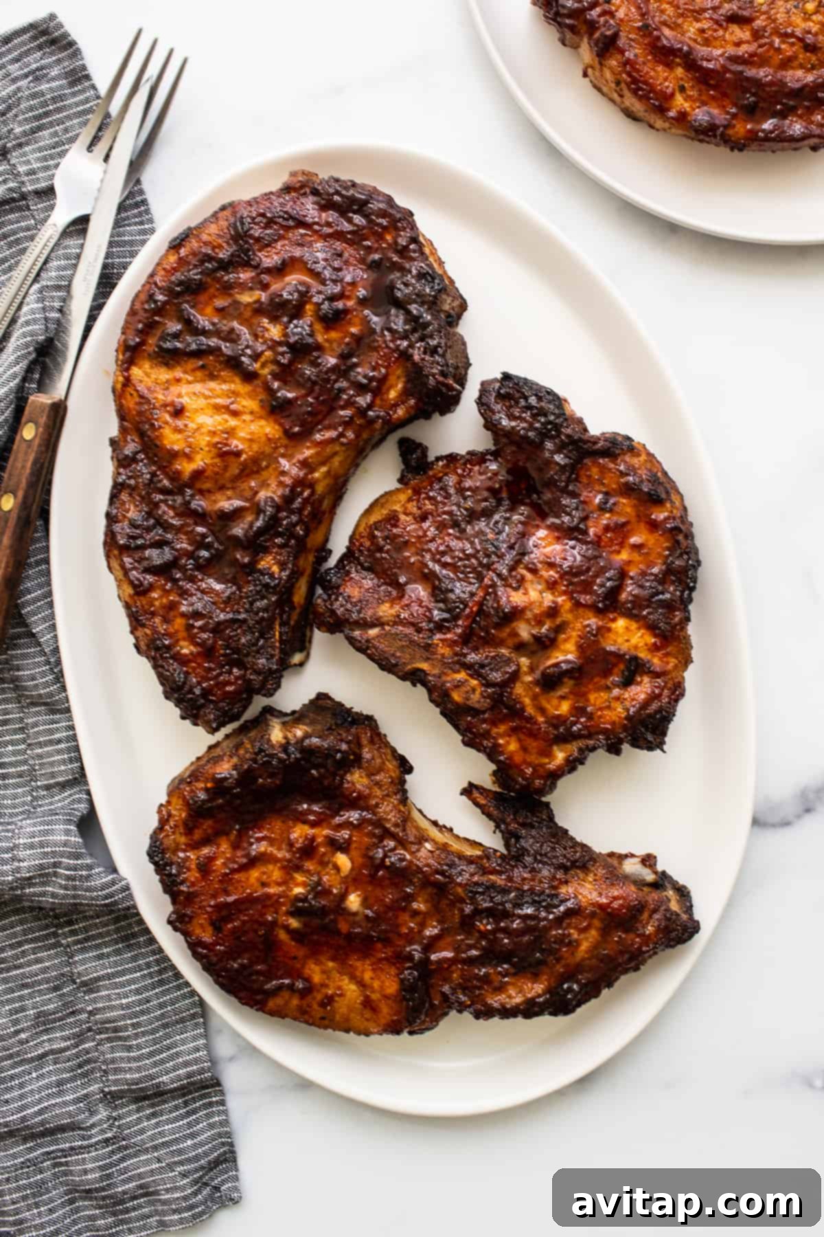 Perfectly cooked, golden-brown air fryer pork chops seasoned with herbs, resting on a white plate with a sprig of fresh rosemary for garnish.