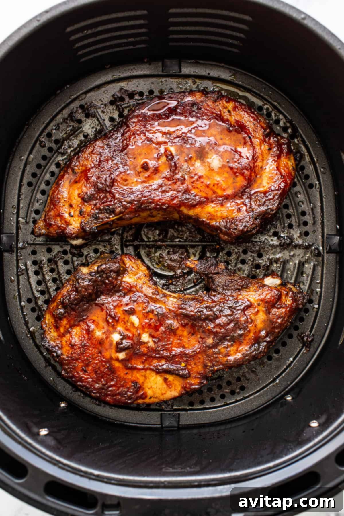 Two perfectly air-fried pork chops, golden brown and juicy, ready to be served from the air fryer basket.