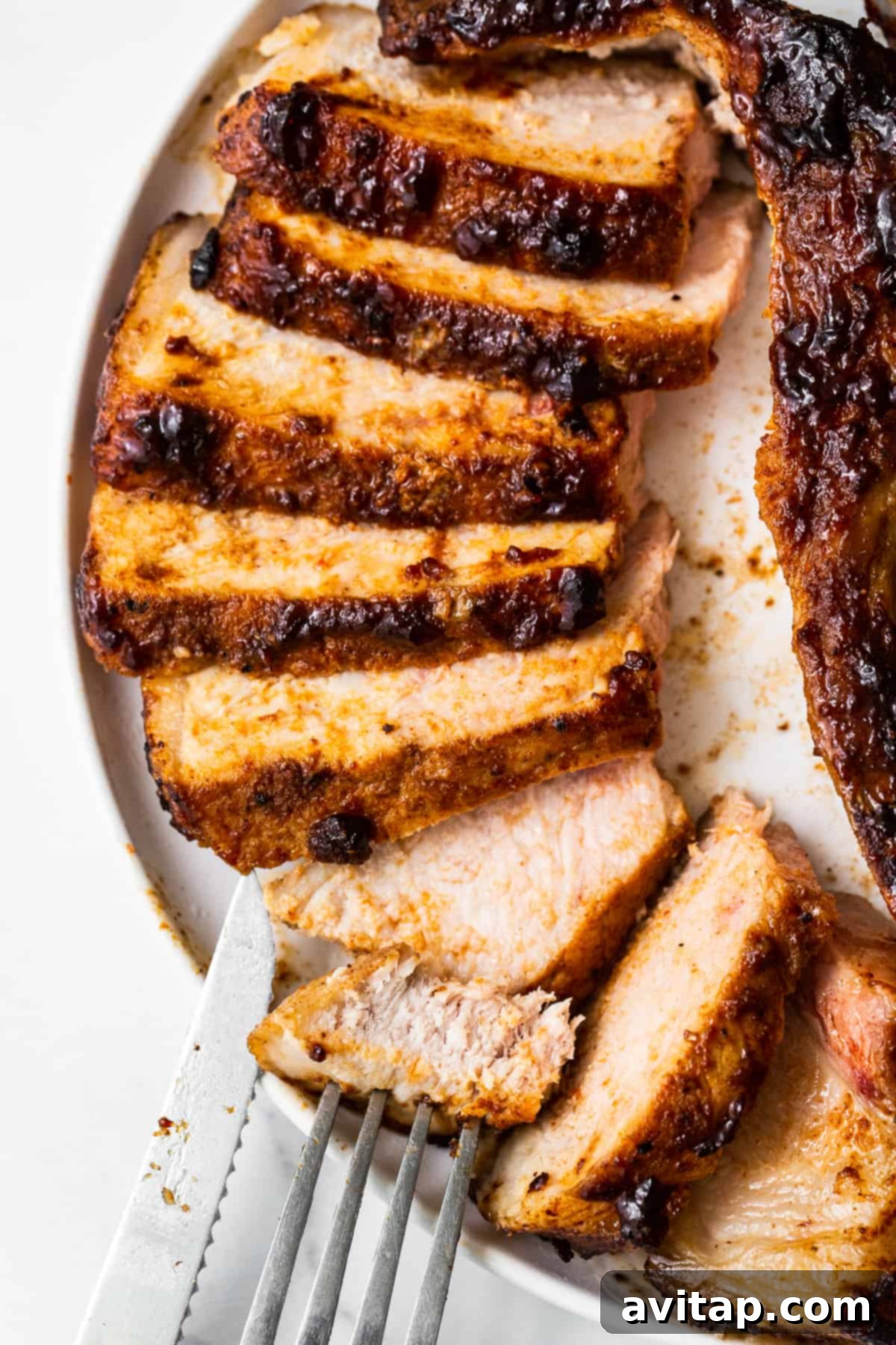 Juicy air fryer pork chops, expertly sliced and arranged on a white serving plate, garnished with fresh herbs.