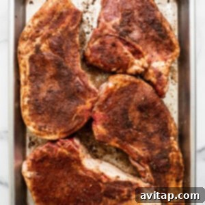 Raw pork chops seasoned with a dry rub, laid on a baking sheet.
