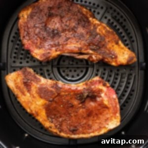 Two pieces of seasoned pork chops cooking inside an air fryer.