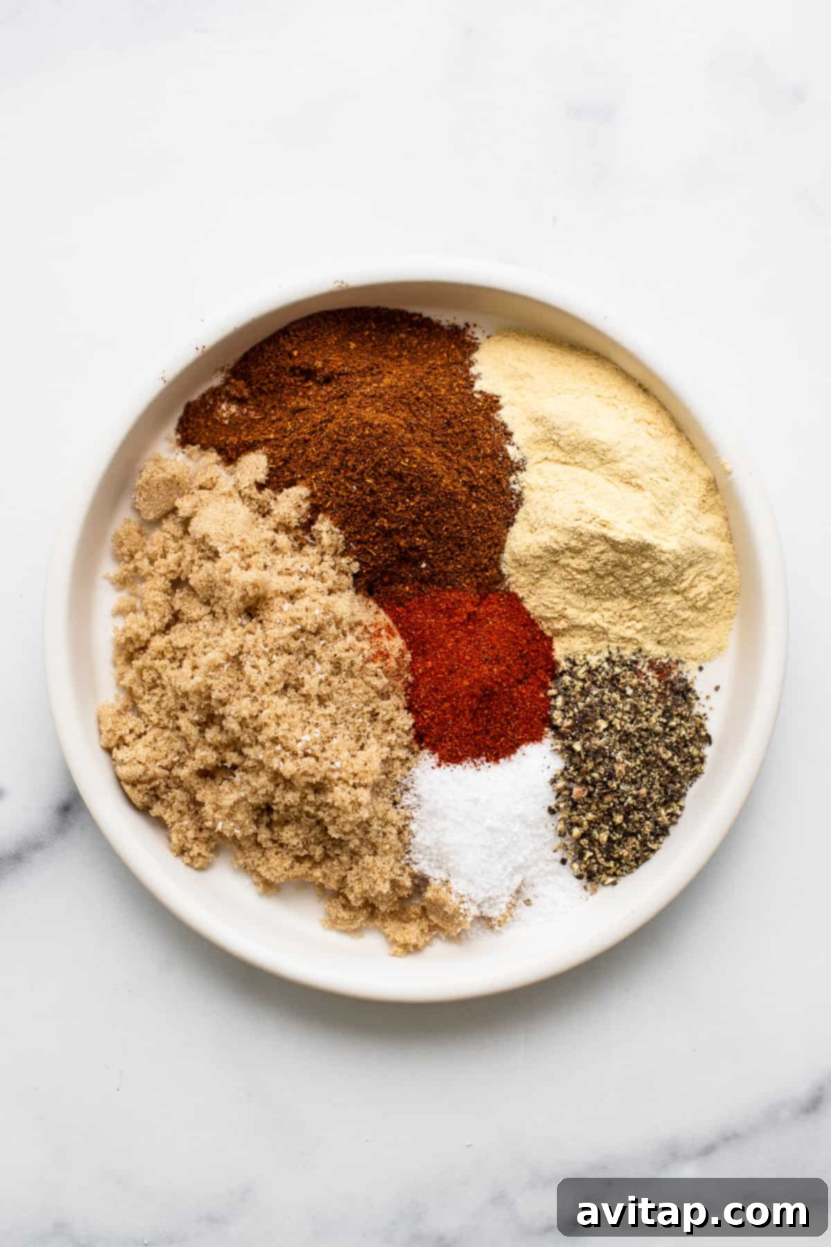 A selection of dry rub ingredients for pork chops, including garlic powder, chili powder, brown sugar, salt, pepper, and paprika, arranged on a rustic plate.