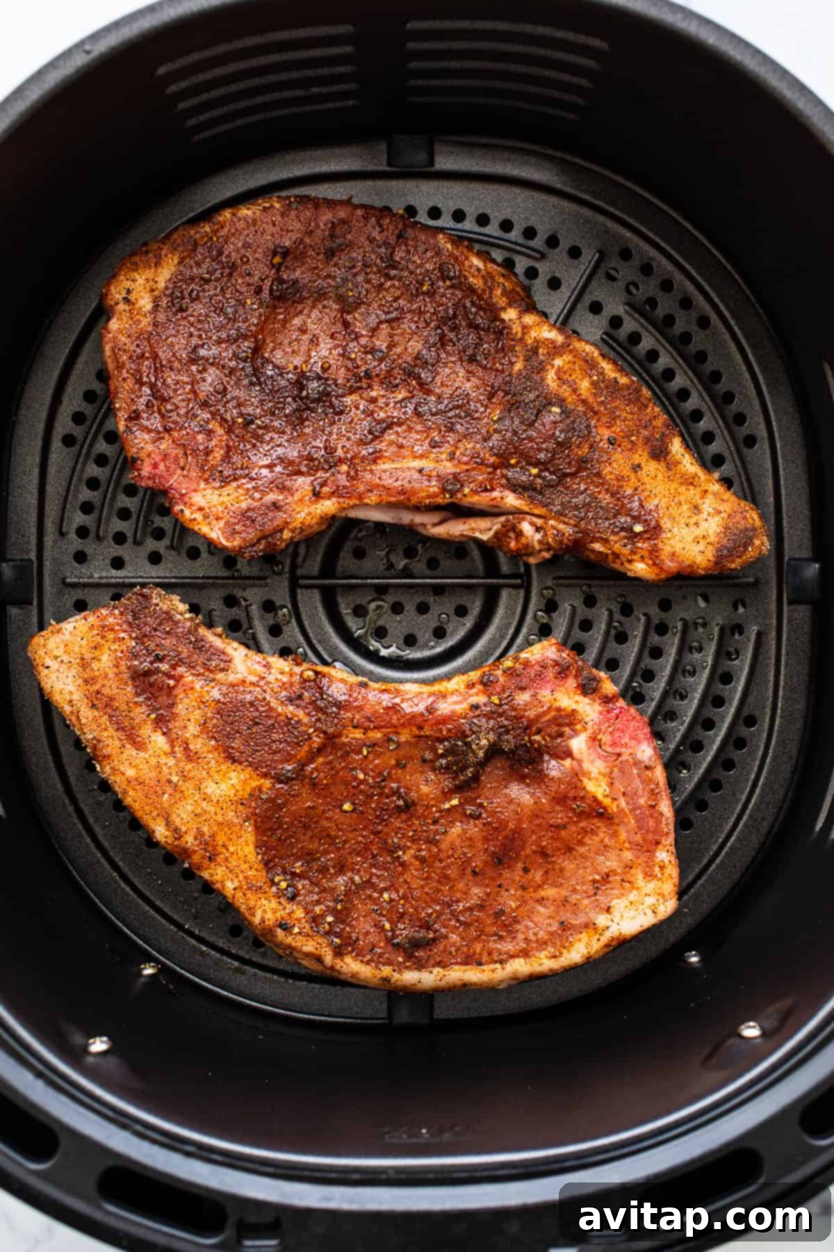 Two perfectly cooked, seasoned pork chops cooking inside an air fryer basket, with visible golden-brown crust.