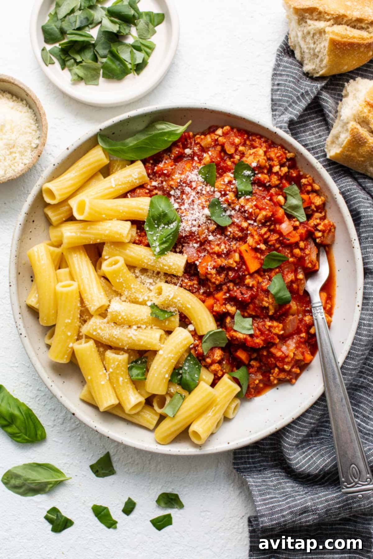 A generous serving of ground chicken bolognese in a bowl, perfectly tossed with pasta and garnished with fresh herbs and Parmesan cheese.