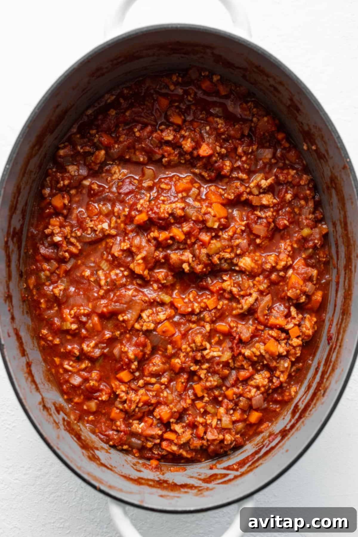 A large pot of ground chicken bolognese, richly colored and simmering, ready to be served over pasta.