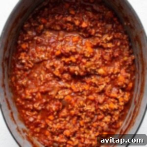 A pot full of ground chicken bolognese simmering slowly in a white pot, deepening its flavors.