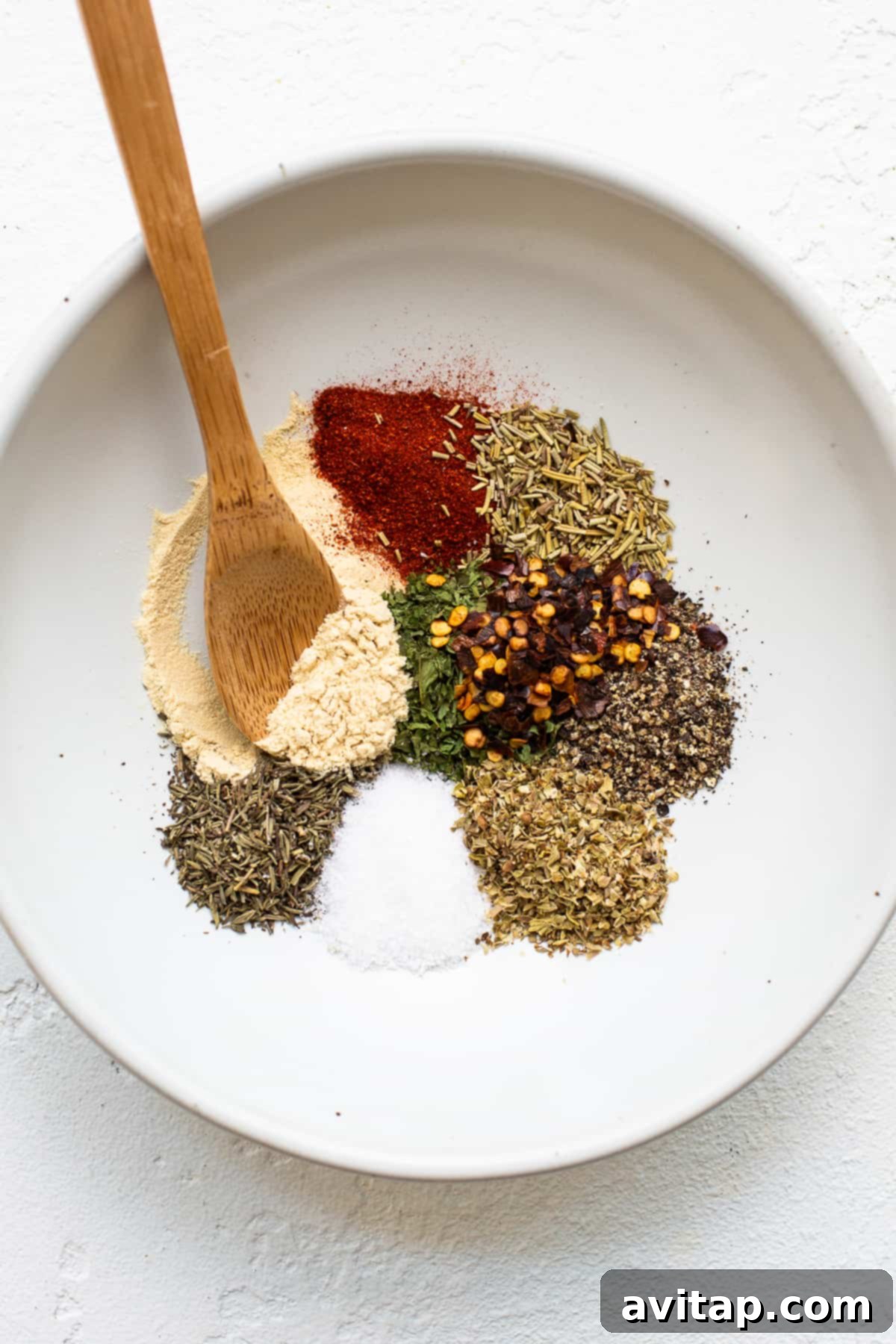 A collection of dried spices, including paprika, thyme, rosemary, parsley, oregano, and red pepper flakes, ready to be blended for the ground chicken bolognese.