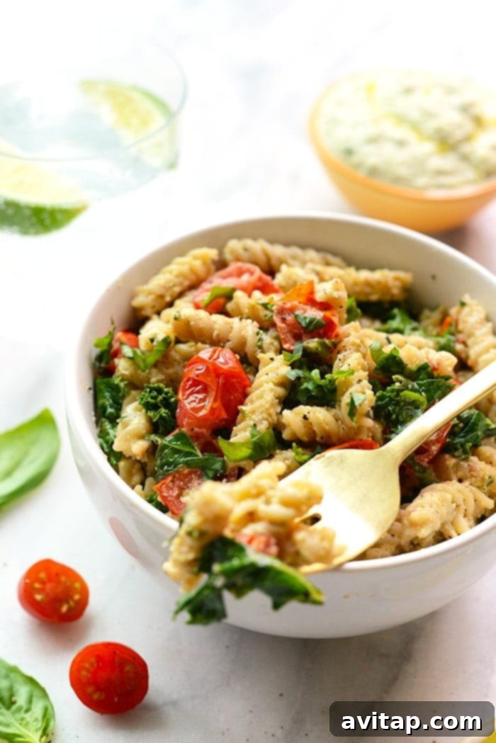 A close-up shot of creamy vegan pasta featuring a rich cashew sauce, vibrant sautéed kale, and sweet cherry tomatoes, ready to be enjoyed.