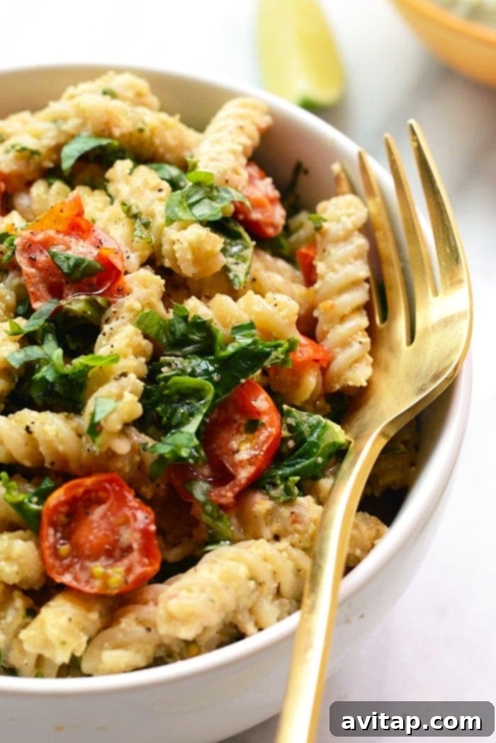 A bowl of creamy vegan pasta with sautéed kale and tomatoes, shown in a clean, minimalist setting, highlighting its fresh ingredients.