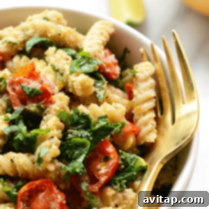 A close-up of creamy vegan pasta salad with vibrant tomatoes and fresh spinach, illustrating the rich texture of the cashew sauce.