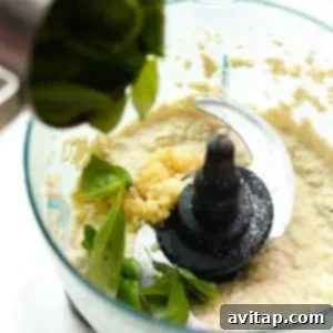A vegan pasta dish topped with a medley of fresh greens and herbs, prepared using a food processor to create its creamy sauce.