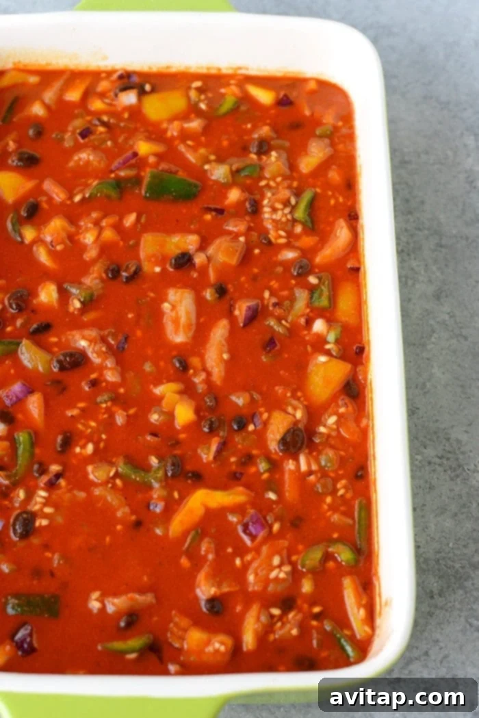 A close-up of a serving of healthy chicken enchilada casserole, garnished with fresh cilantro and a dollop of sour cream, on a white plate.