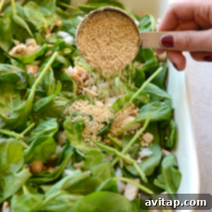 A person adds sesame seeds to a spinach salad.