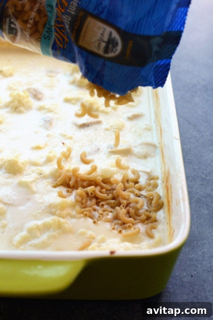 Creamy Cauliflower Chicken Mac and Cheese 3 Gluten-free macaroni noodles being poured into a casserole dish, ready for baking.