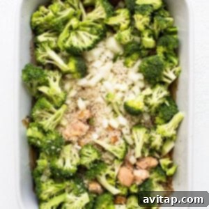 Uncooked chicken, rice, onion, and broccoli mixed in a casserole dish.