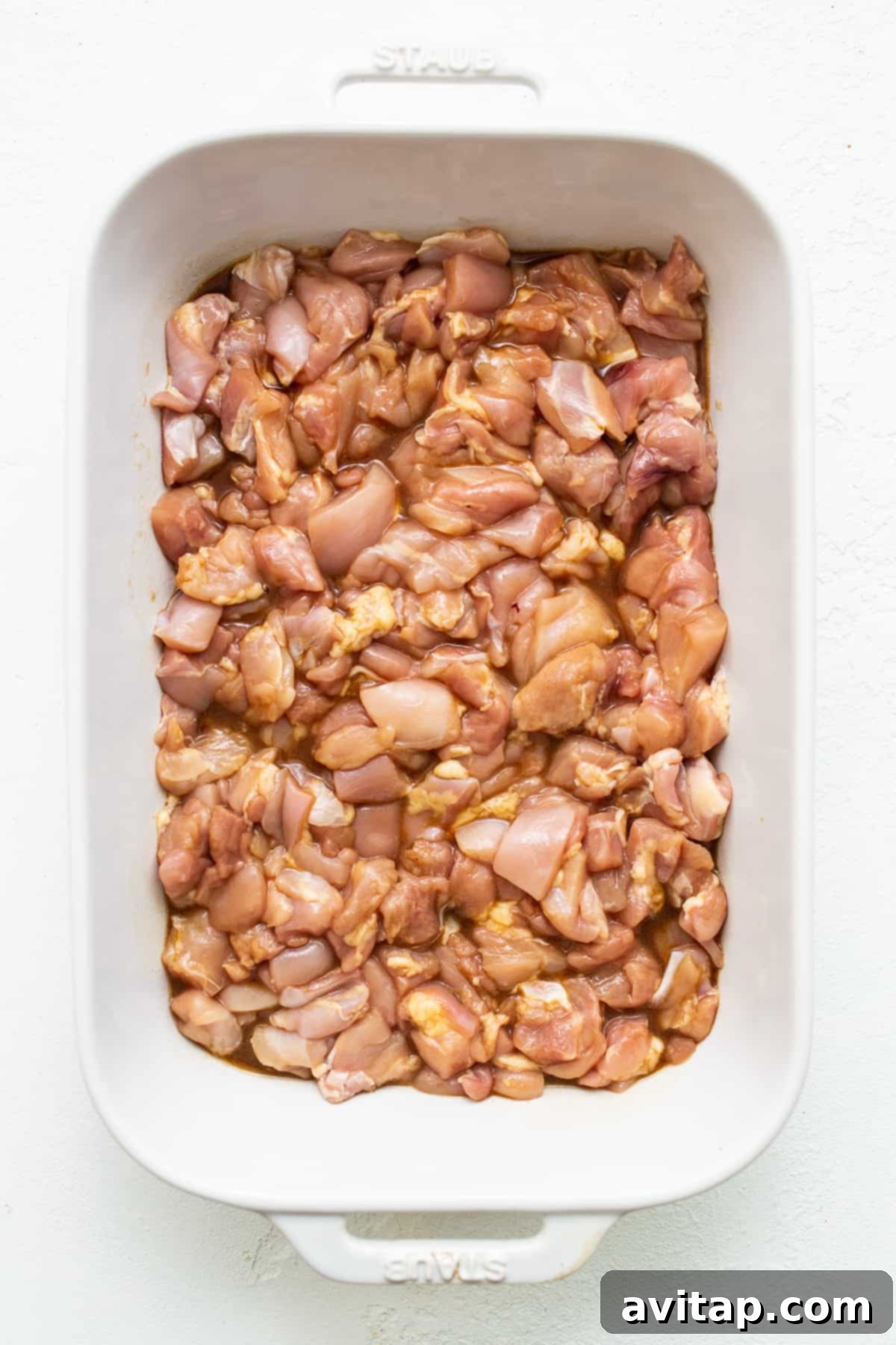 Prepping the chicken for a flavorful Orange Chicken Casserole. Chicken chunks marinating in a casserole dish with a savory orange sauce.