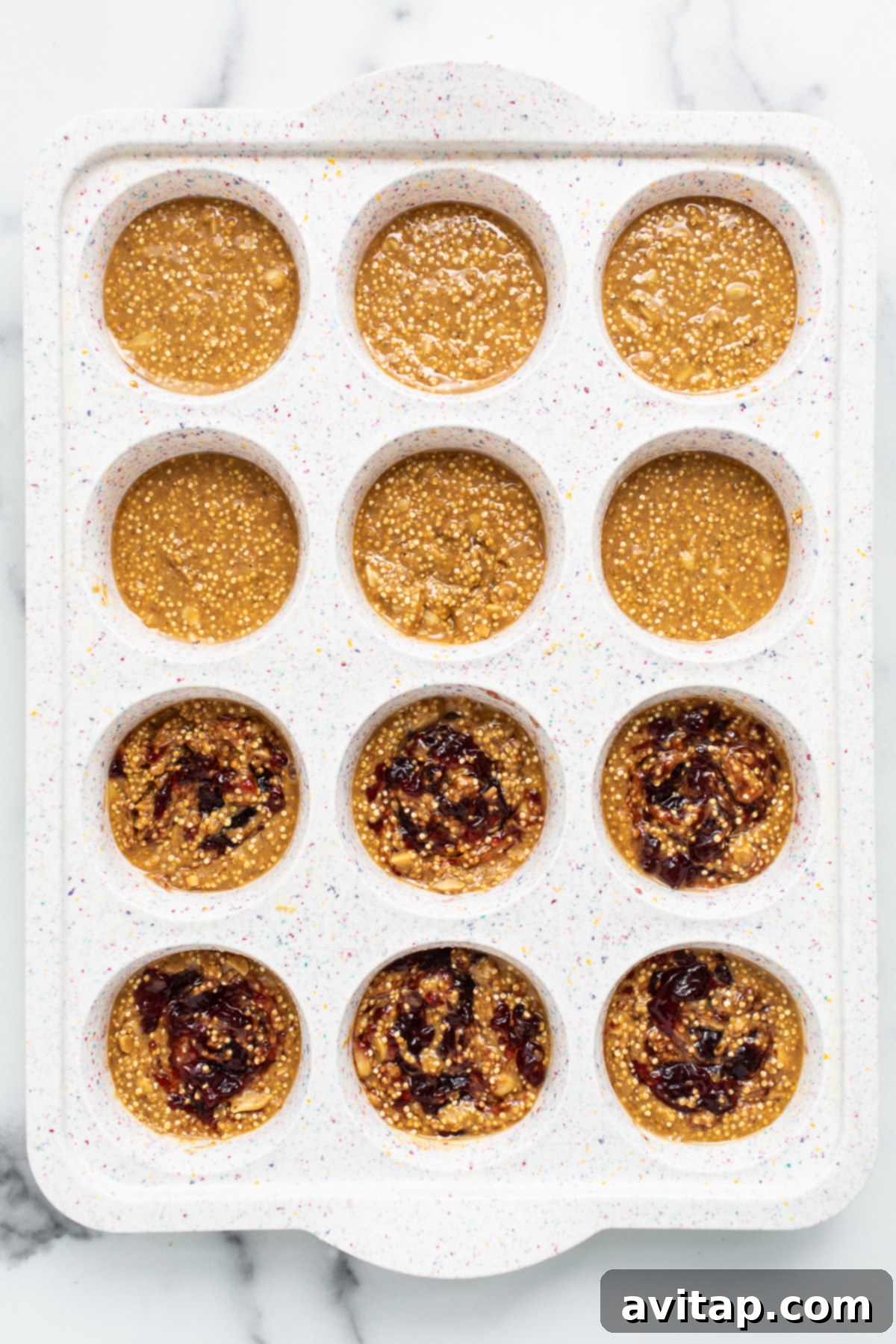 Peanut butter and jelly quinoa cups carefully arranged in a muffin tin, ready for freezing.
