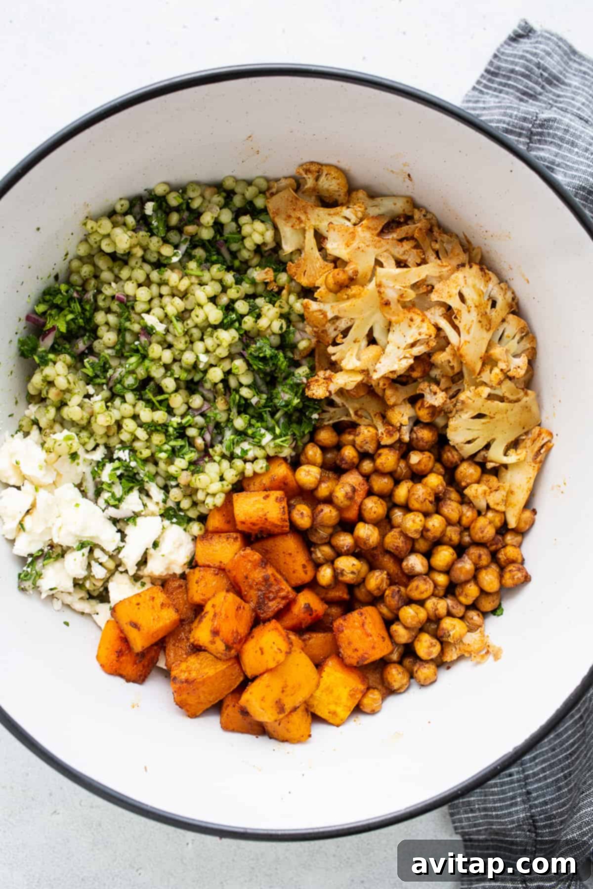 Israeli Couscous Medley 3 A close-up shot of seasoned chickpeas, butternut squash, and cauliflower on a baking sheet, ready for roasting.