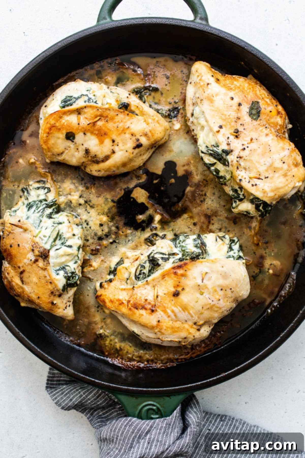 Two spinach stuffed chicken breasts searing in a hot cast-iron skillet, developing a golden crust.