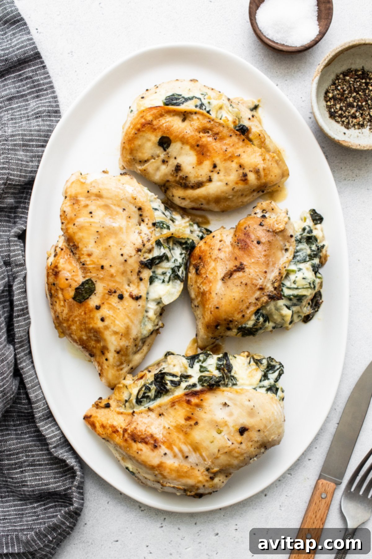 A whole spinach stuffed chicken breast presented on a white plate with fresh herbs, ready to be enjoyed.