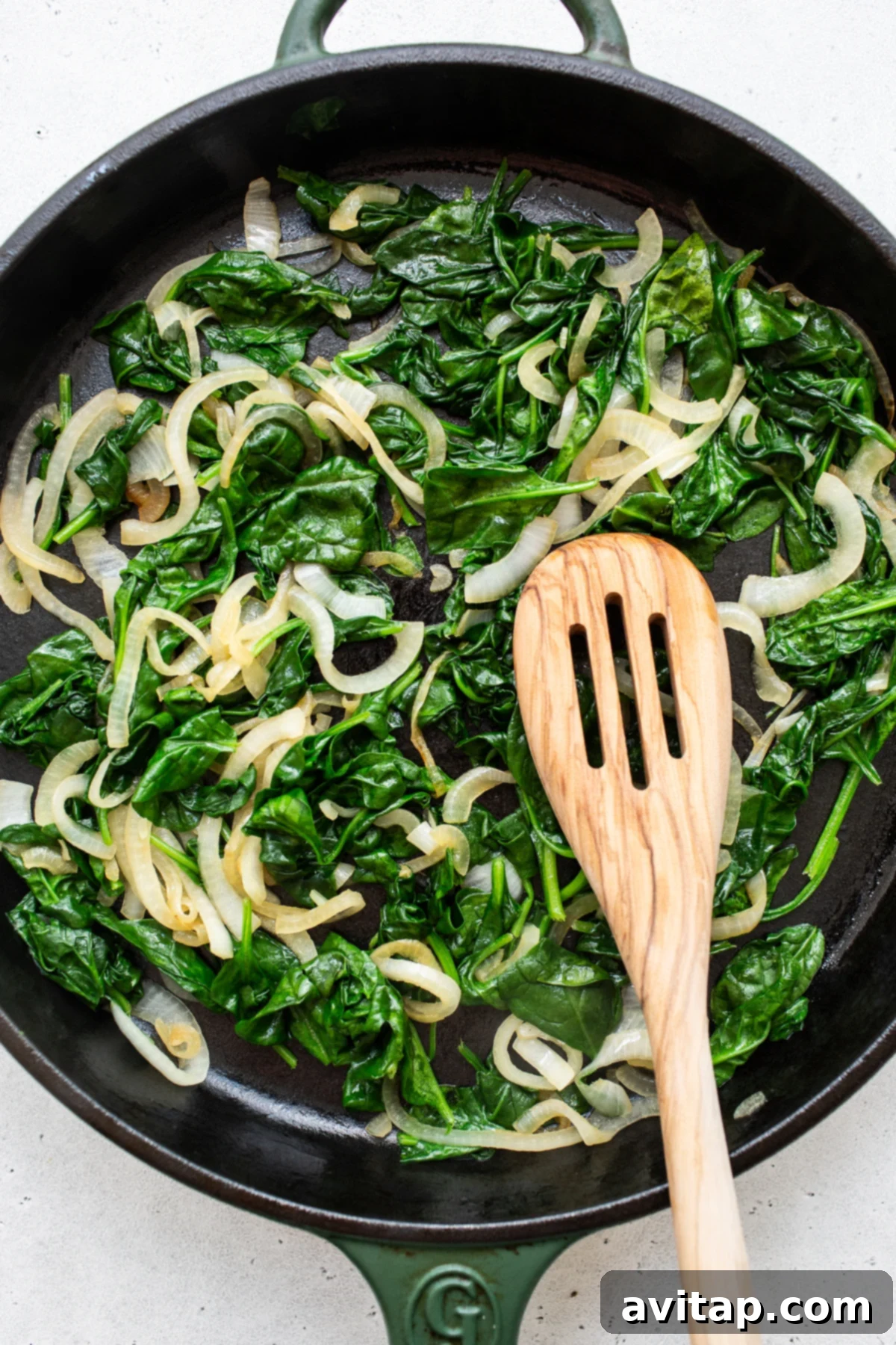 Fresh spinach and sliced onions being sautéed in a skillet, creating a fragrant base for the filling.