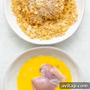 Chicken thighs being breaded in a bowl with eggs and cornflake mixture.