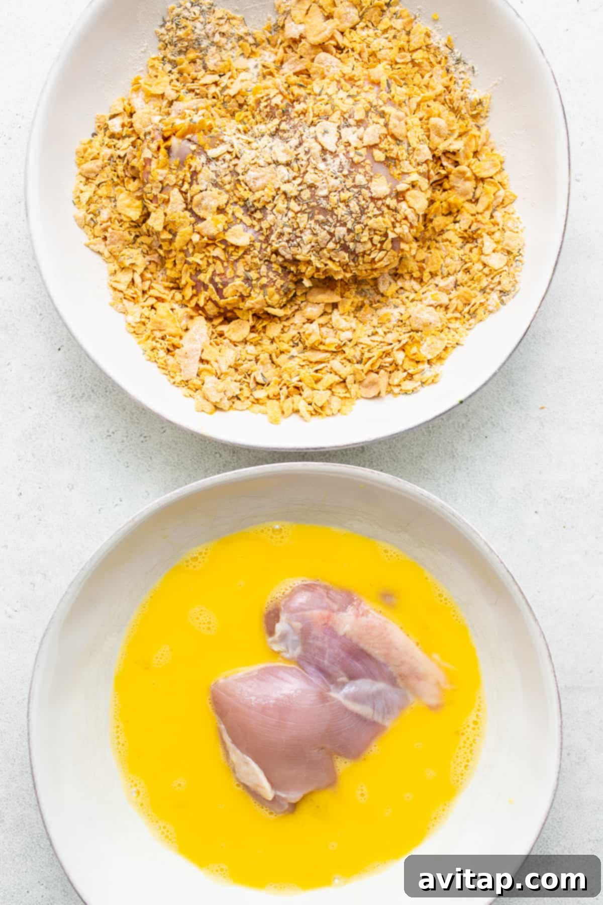 Boneless, skinless chicken thighs being breaded with cornflake mixture.