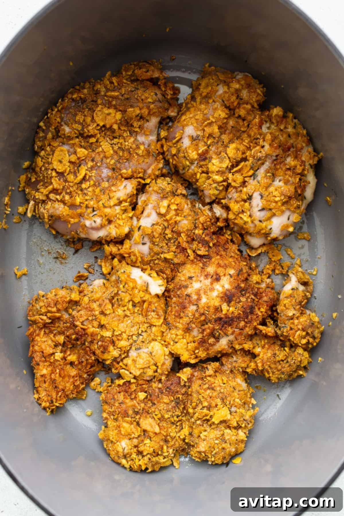 Breaded chicken thighs being seared to a golden brown in a cast-iron skillet.
