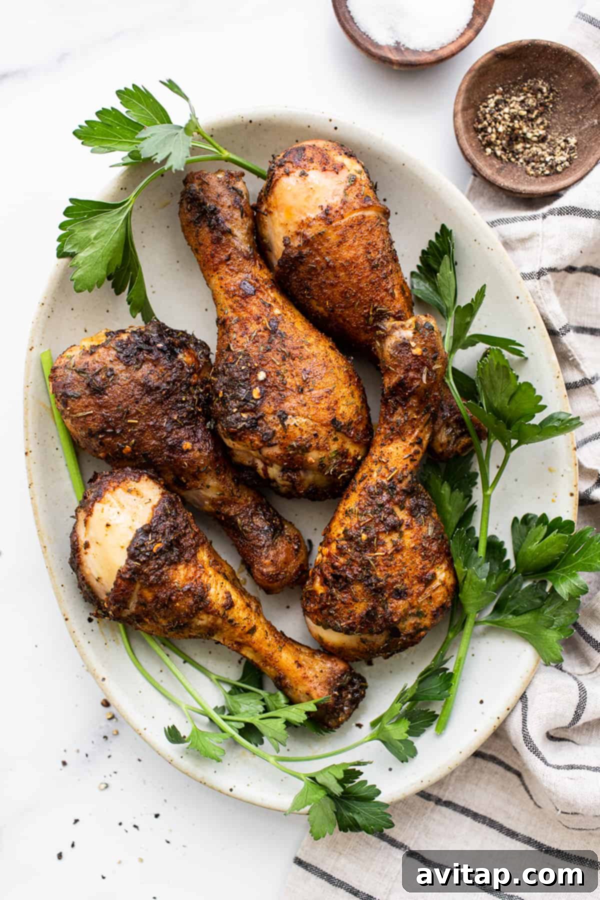 A close-up of several perfectly baked chicken legs on a white plate, showcasing their crispy, golden-brown skin.