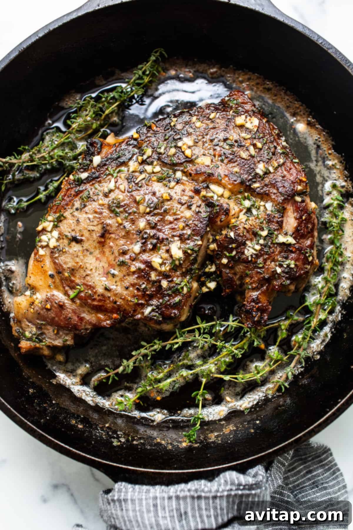 Perfect Cast Iron Steak 2 A perfectly seared cast iron steak resting in the pan with garlic and herbs.