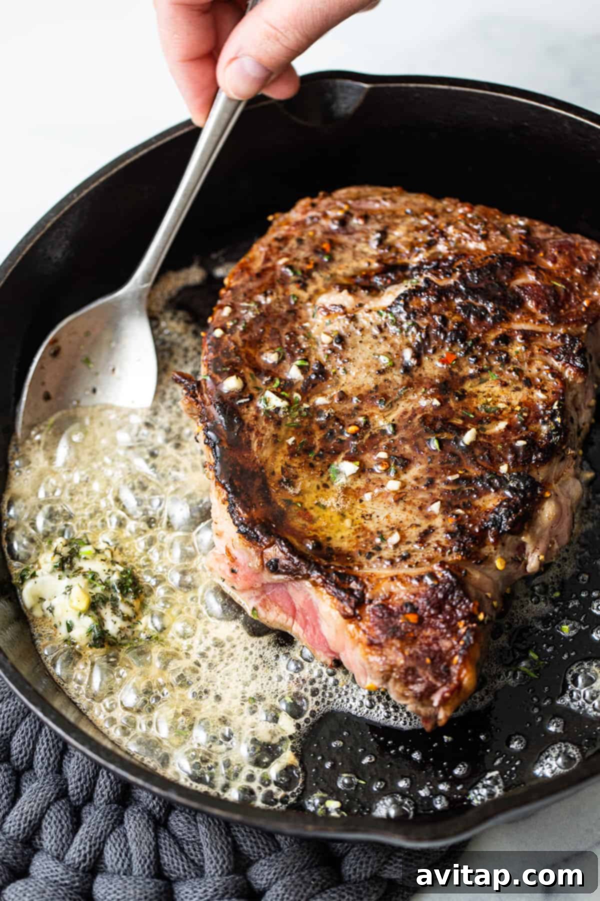 Perfect Cast Iron Steak 6 A spoon basting a sizzling steak with melted butter in a hot cast iron skillet.