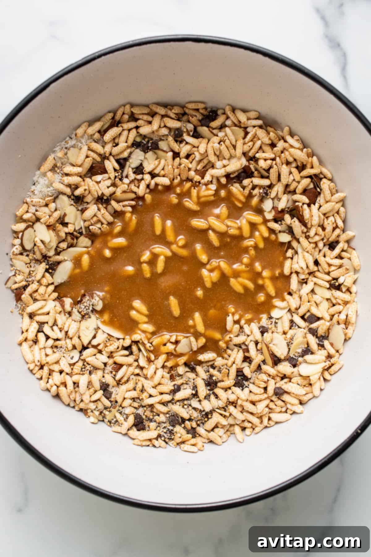 Melted brown rice syrup mixture with brown rice being stirred in a bowl, forming a gooey chocolate coating.