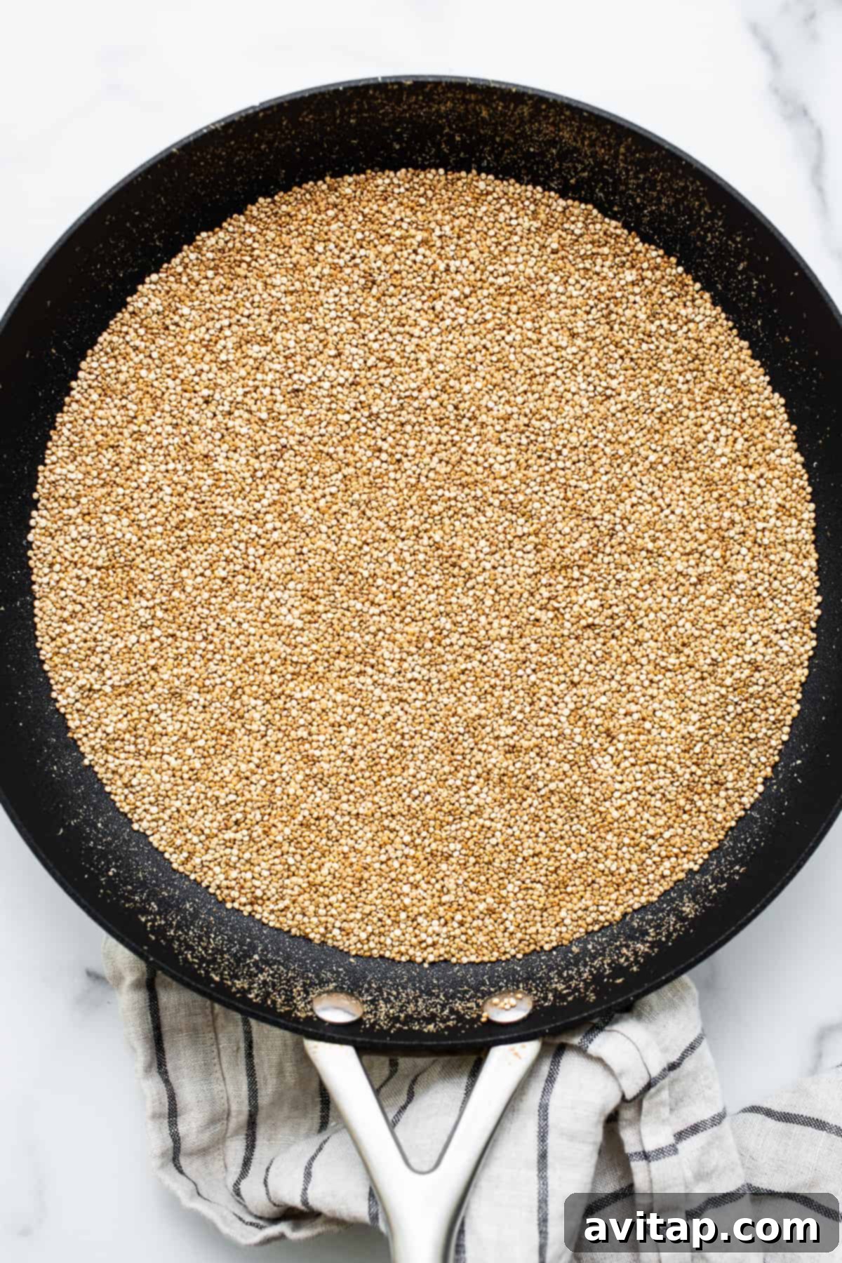 White quinoa being puffed in a hot skillet, showing the initial stages of toasting and popping.