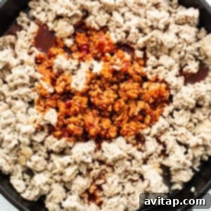 Spicy gochujang sauce being added to browned ground chicken in a hot skillet.