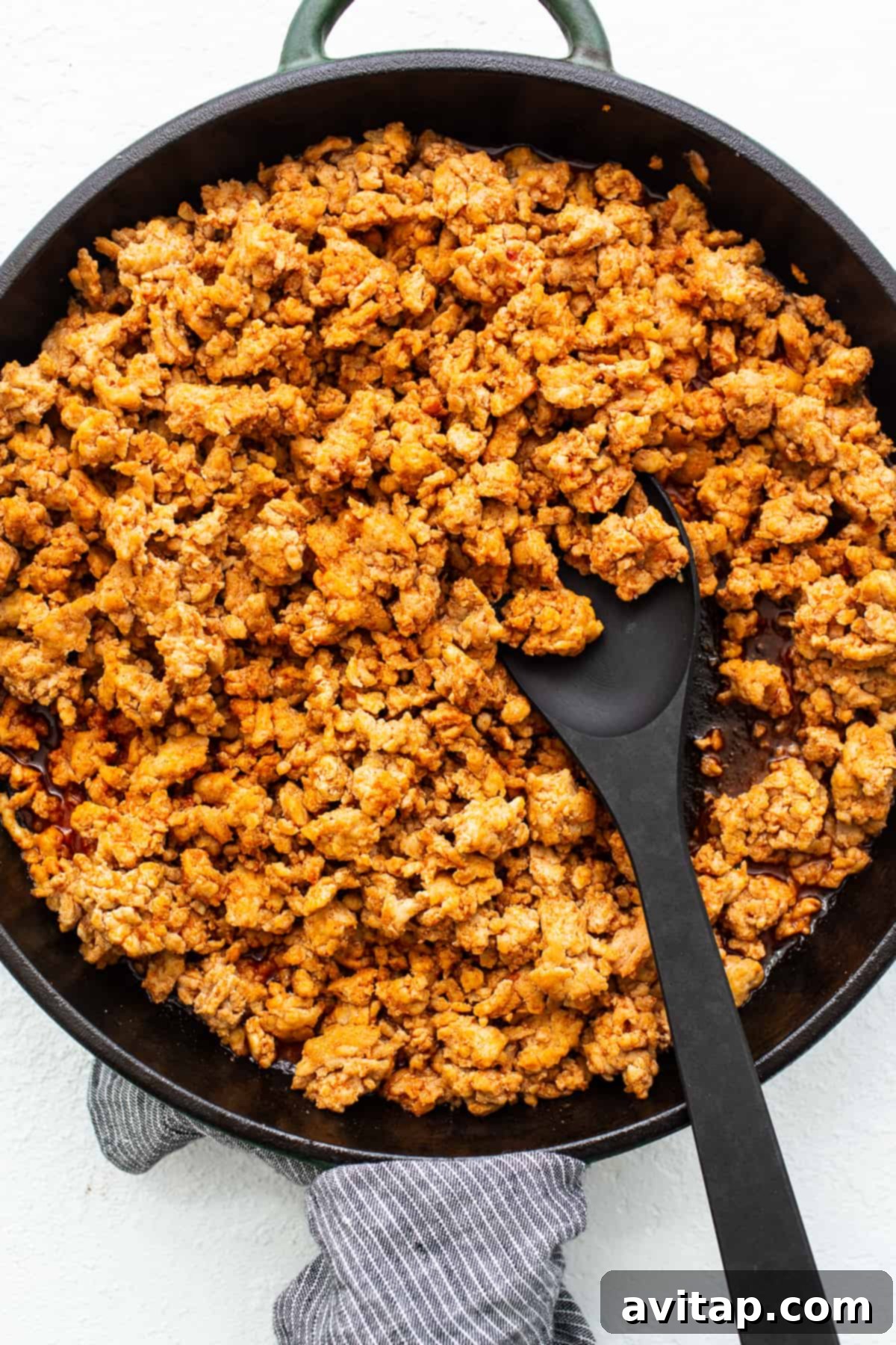 A close-up shot of saucy ground chicken being spooned from a skillet, highlighting its rich color and texture.