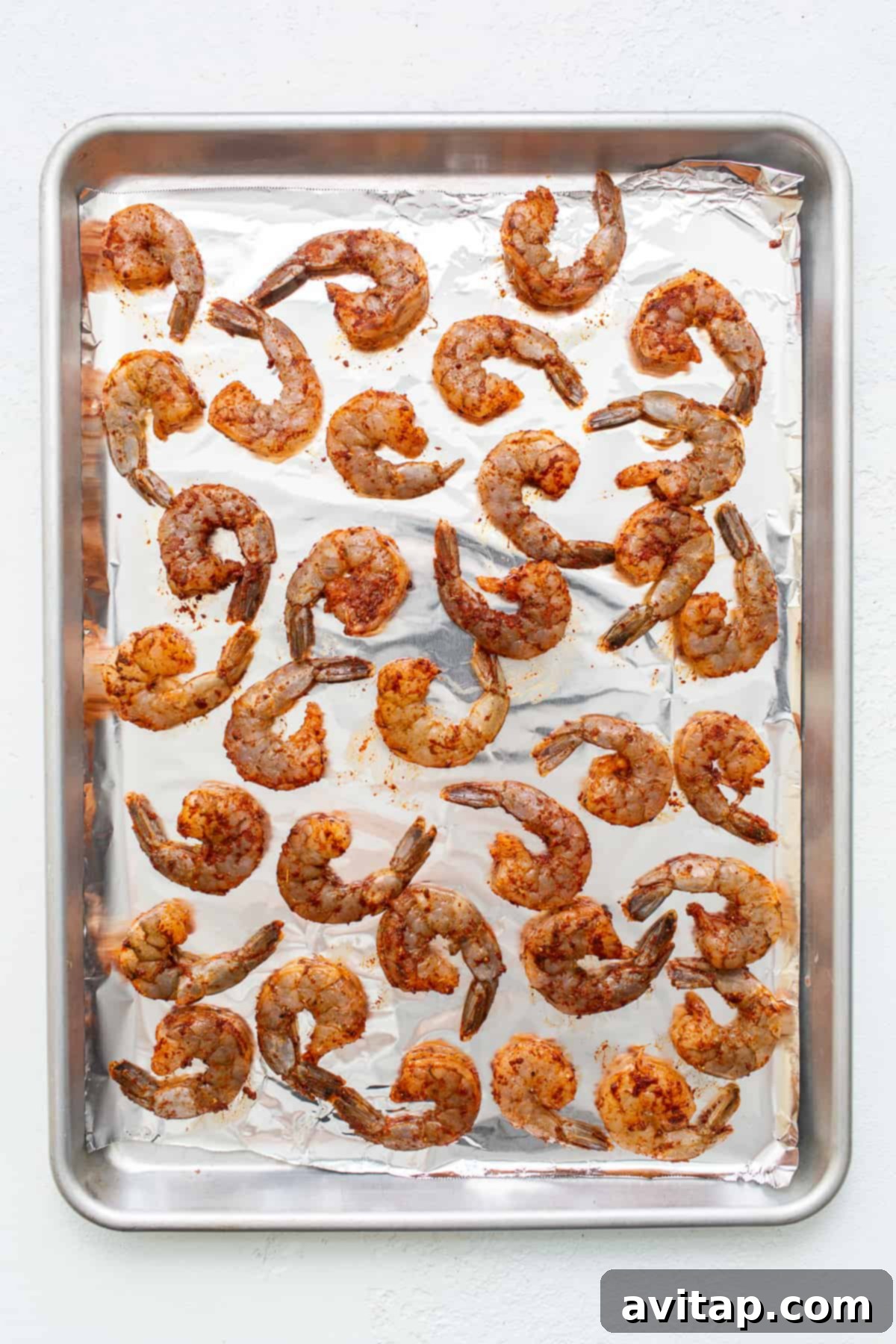 Seasoned shrimp on a baking sheet prepared for broiling. Seasoned raw shrimp meticulously arranged on a baking sheet, ready for broiling.