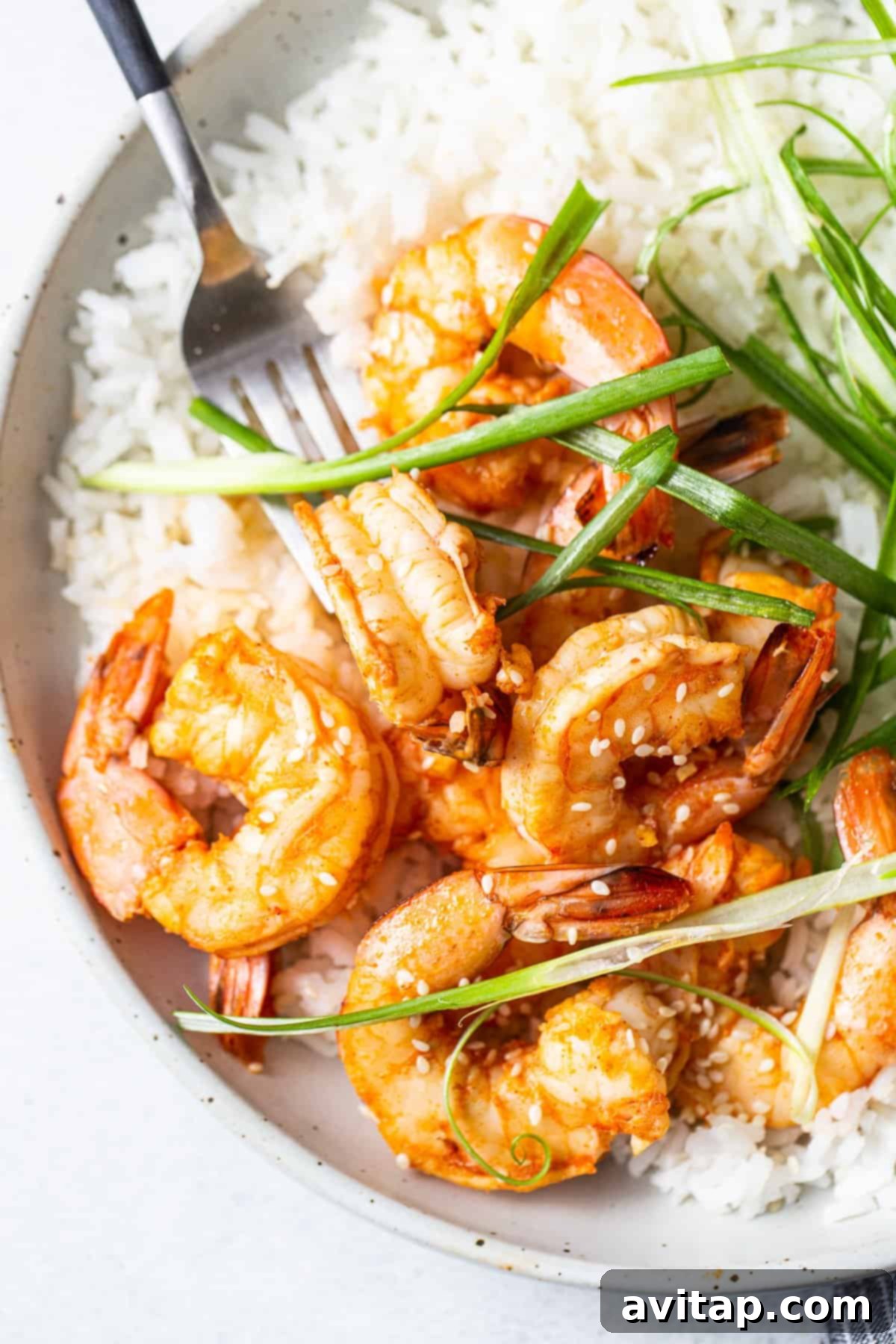 Spicy Garlic Prawns and Rice A close-up of a bowl of spicy garlic prawns with rice, garnished with green onions.