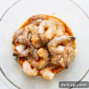 Raw shrimp marinating in a glass bowl.