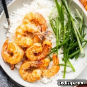 A bowl of rice topped with cooked shrimp and green onions.