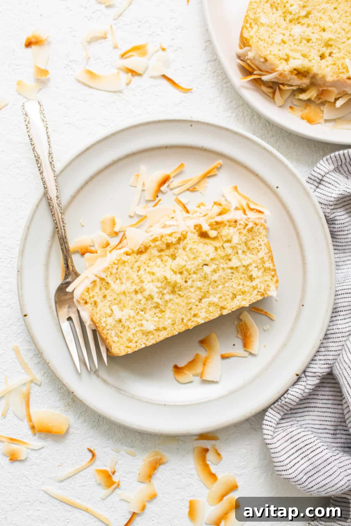 A perfectly sliced coconut loaf cake on a plate, showcasing its moist texture and glistening glaze.