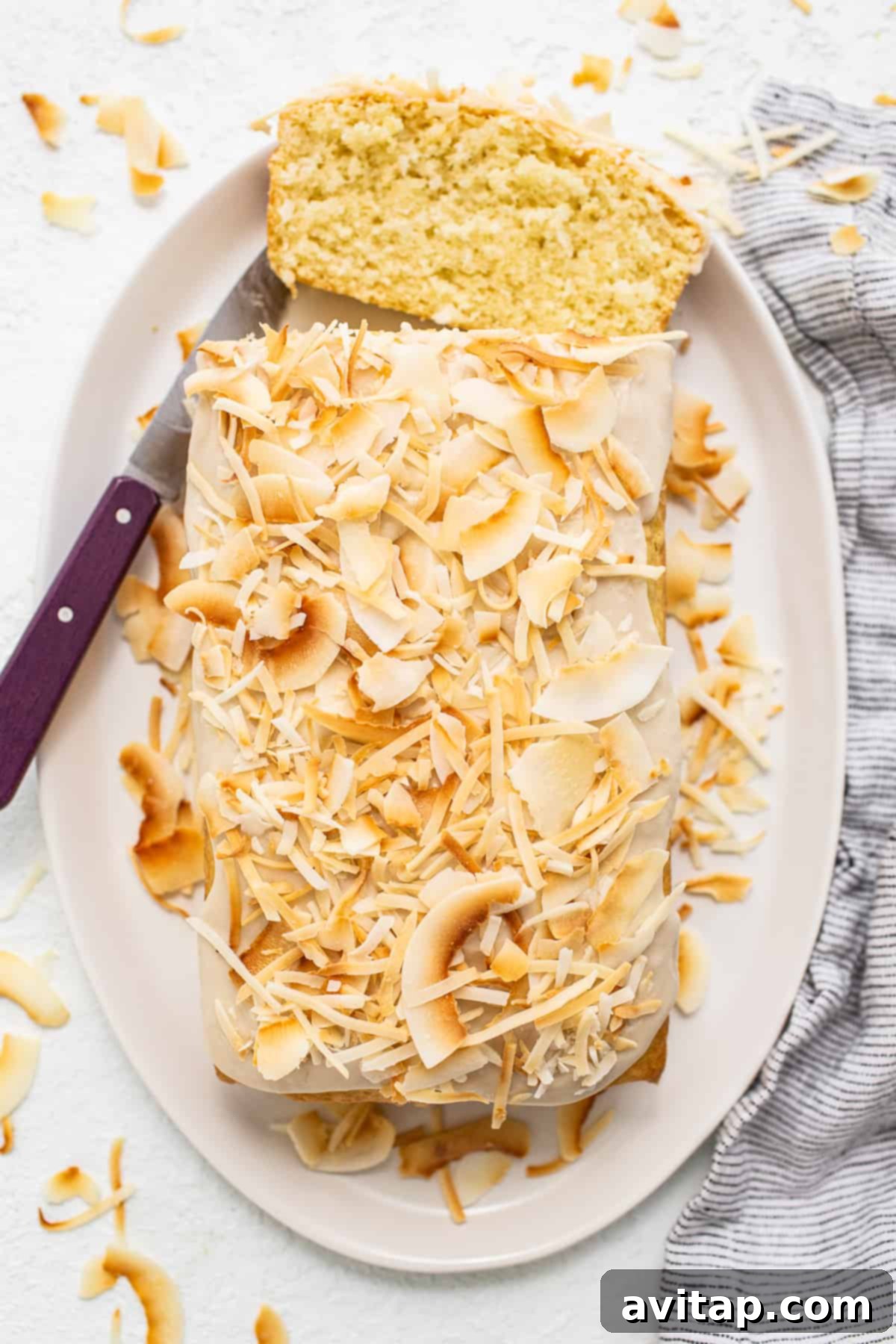 A perfect slice of moist coconut loaf cake displayed on a simple white plate, invitingly ready to be enjoyed as a delightful treat.